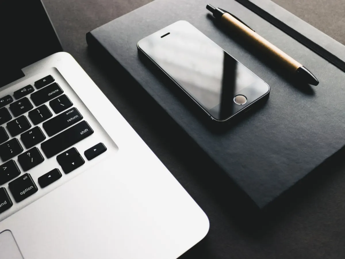 Portable, cellulaire, bloc note et crayon déposés sur un bureau