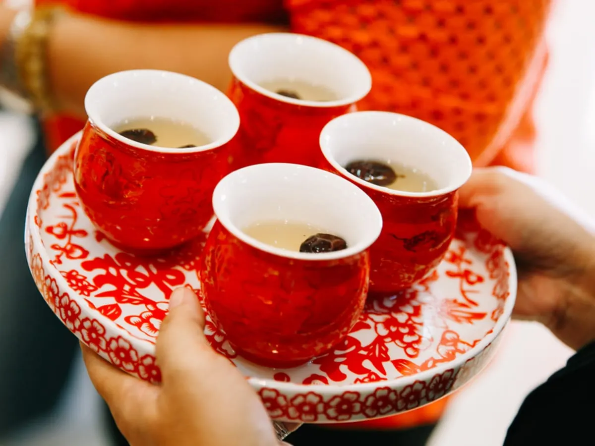 Une personne porte un plateau rond sur lequel sont posées 4 petites tasses de thé.