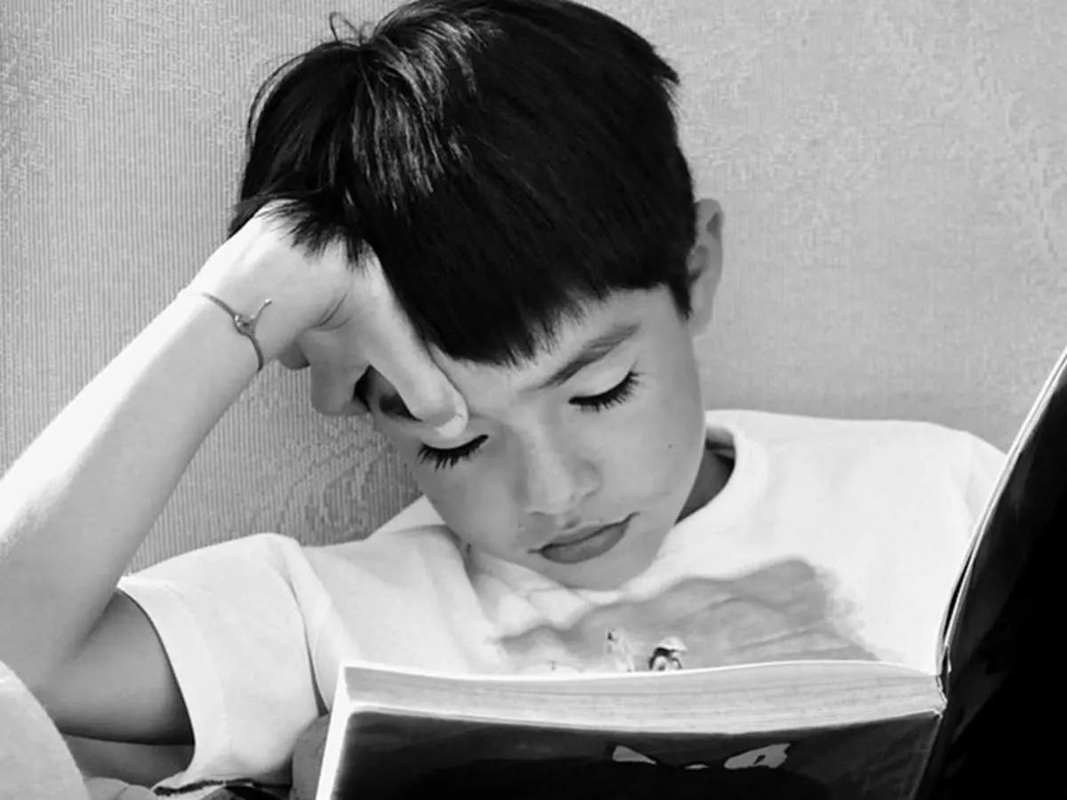 Photo en noir et blanc d'un enfant qui lit un livre.