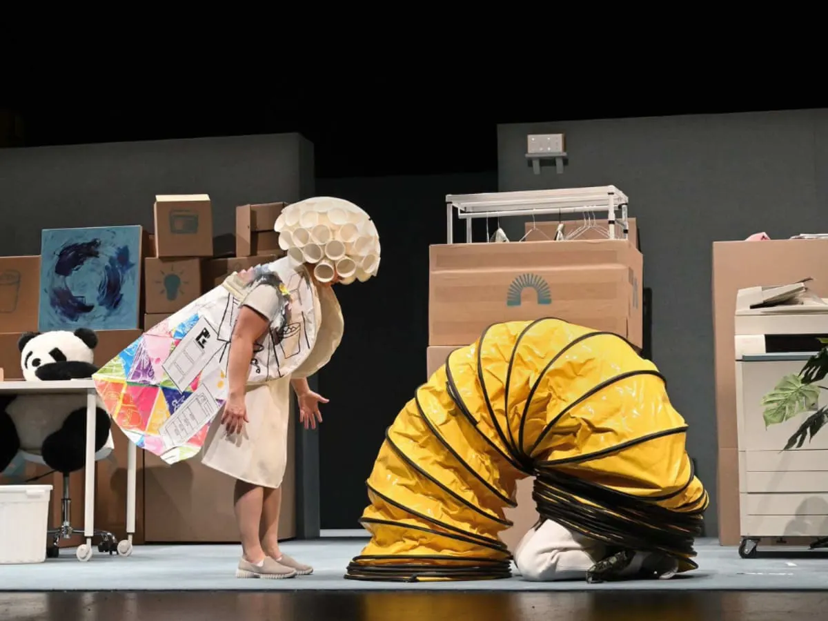 Deux acteurs en costumes farfelus, avec comme décor des boîtes de carton.