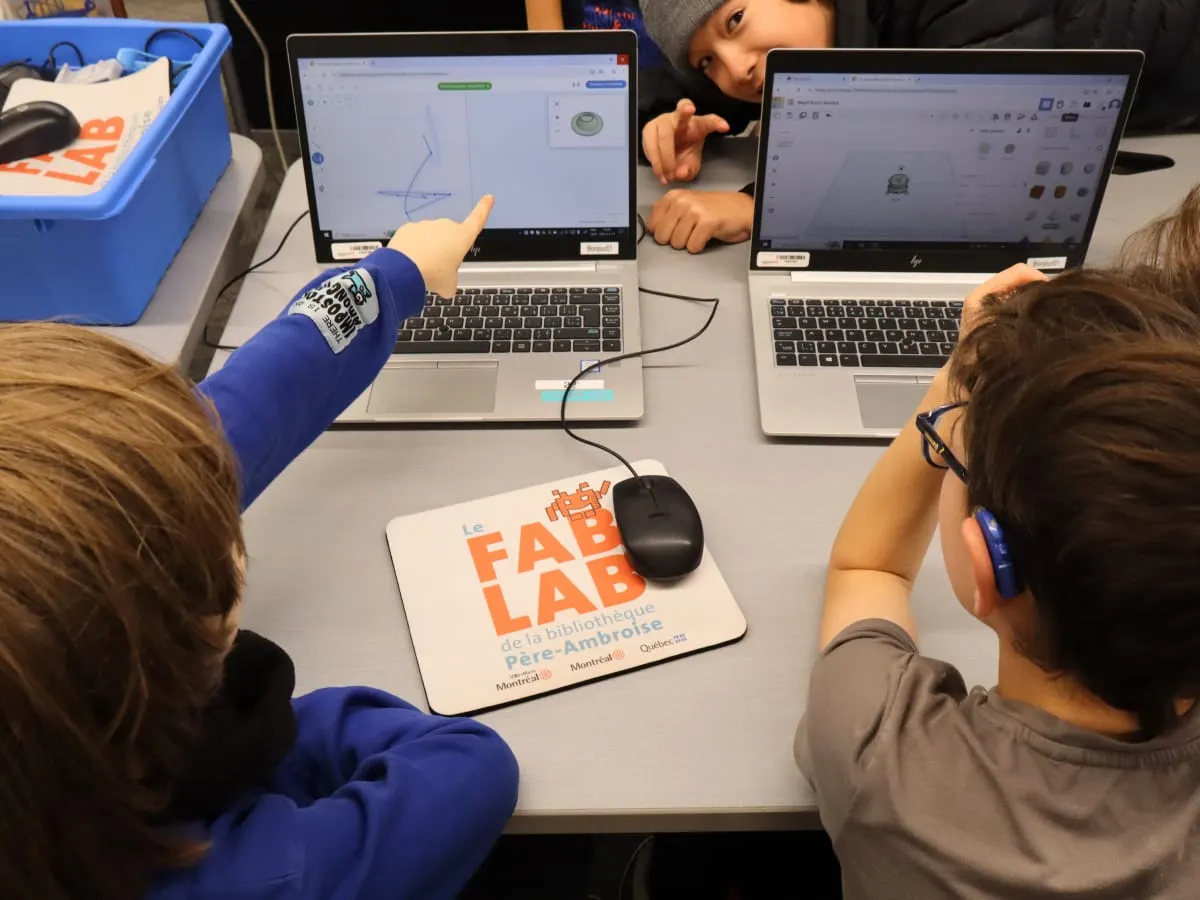 Deux enfant travaillent à l'ordinateur et se poitent l'écran. On voit des formes géométriques sur leur logiciel e modélisation 3D.