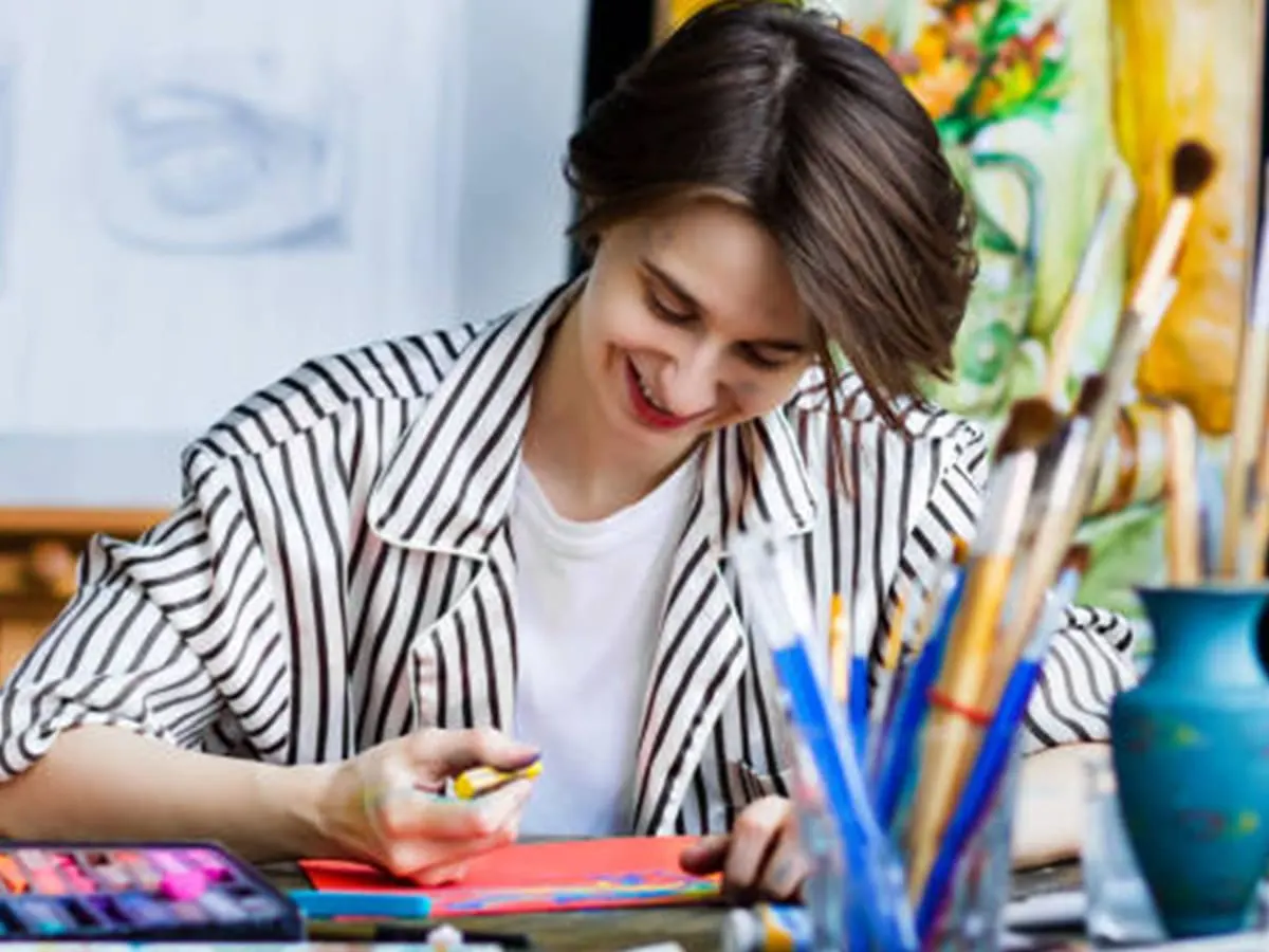 Une personne souriante en train de dessiner, dans un atelier d'artiste.