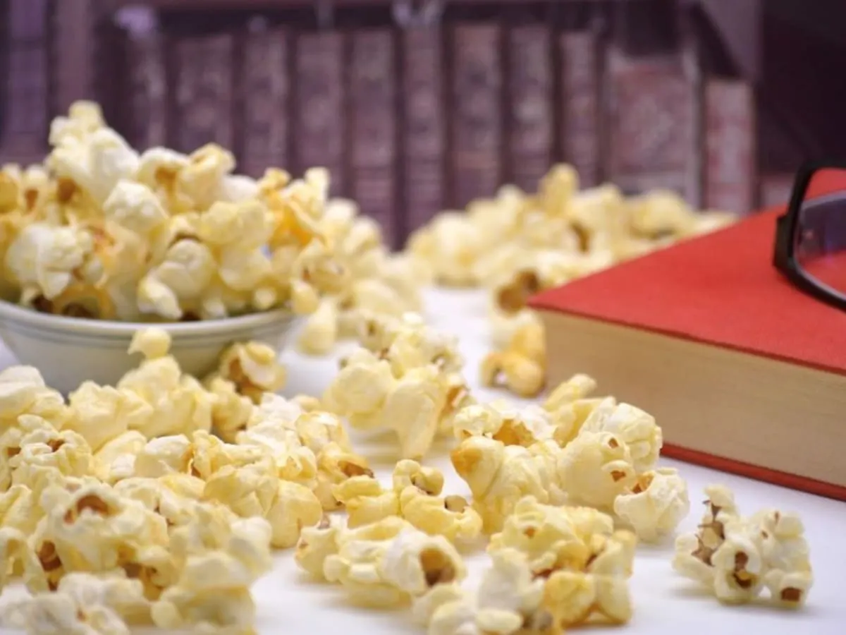 Bol de popcorn avec un livre et des lunettes sur une table.