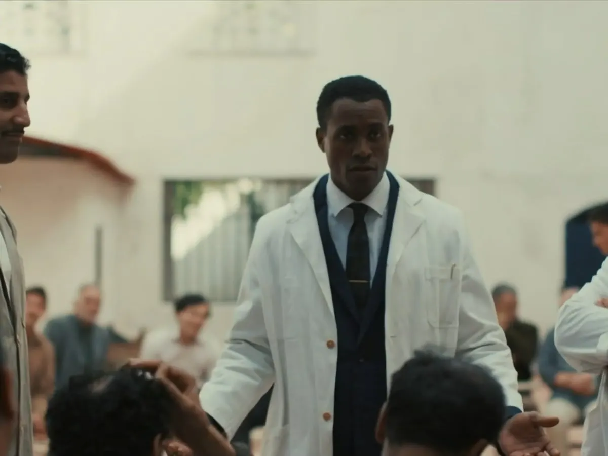 La photo montre le personnage de Frantz Fanon au centre, au milieu d''un cercle de personnes