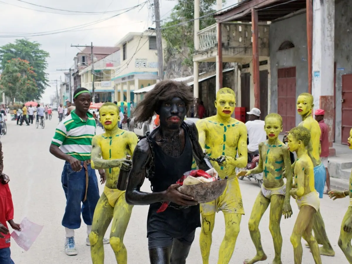 Scène de rue en Haïti. Des personnes peintes en jaune de la tête au pied marche derrière une personne habillé en noir tenant un panier